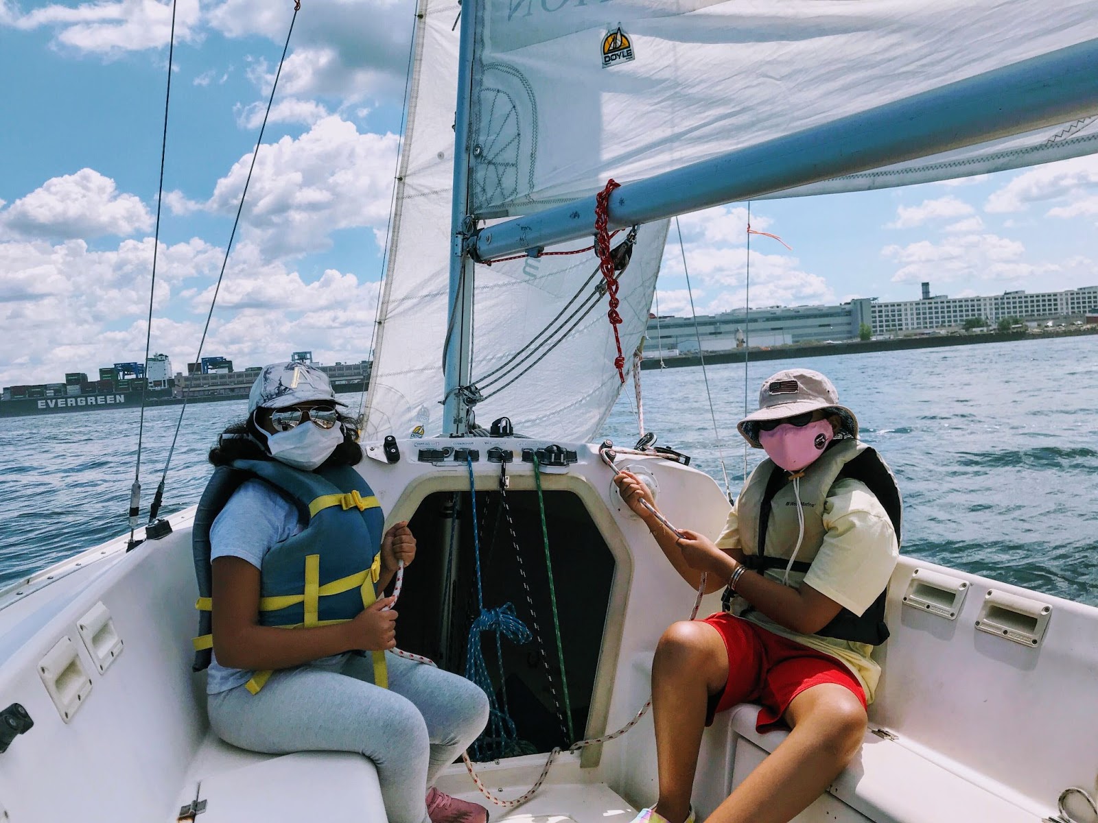 Two women wearing faces masks and life jackets sitting on a boat in the ocean on a sunny day.