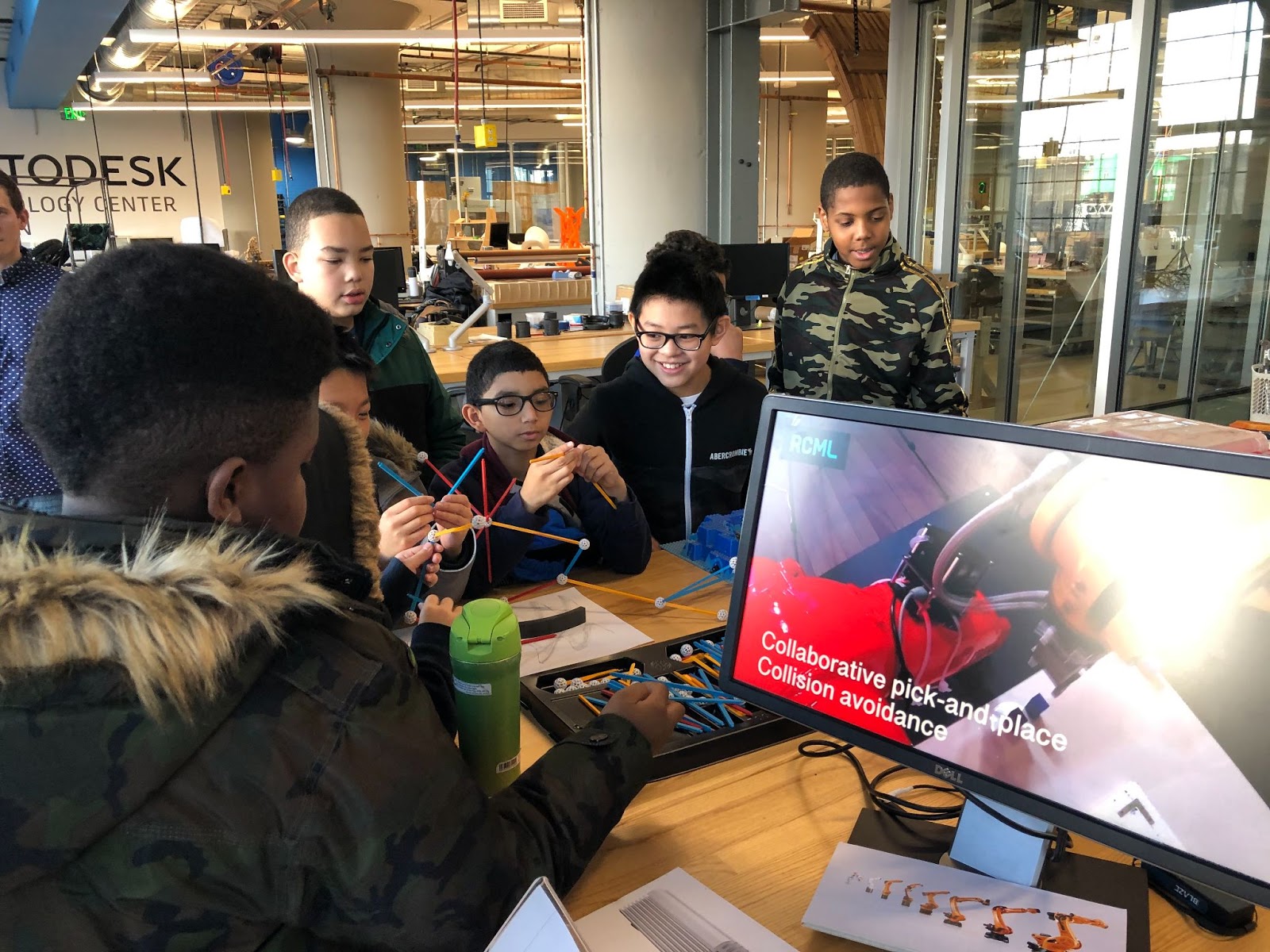 A group of young boys sitting around a table at a technology center building a model of a molecule. There is a computer on the table. 